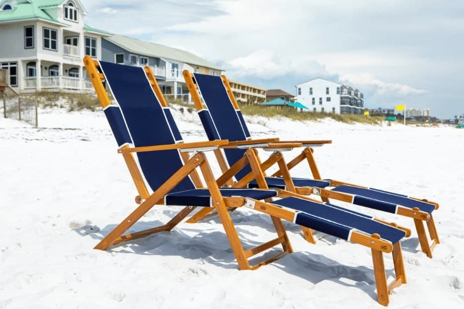 Wooden beach lounge chairs on white sand near coastal homes
