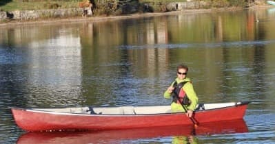 Solo canoeist paddling on calm reflective lake at sunrise