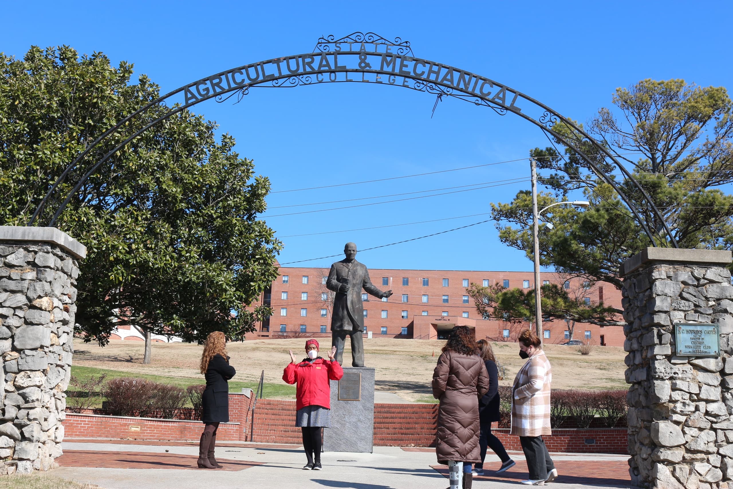 Campus gateway and statue with visitors on outdoor history tour