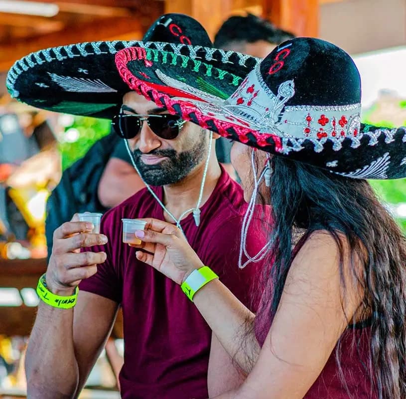 Couple wearing sombreros sampling tequila at outdoor event