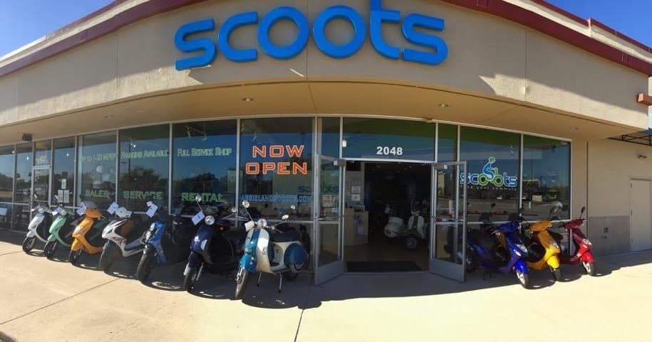 Scooter shop exterior with row of scooters under daytime sky