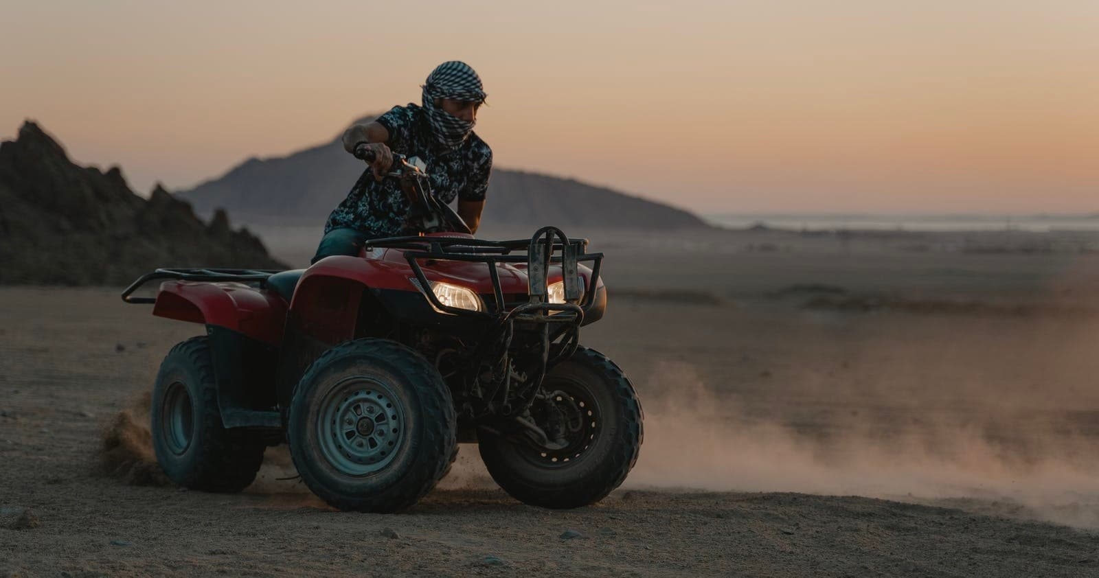 ATV rider kicking up dust on desert dunes at sunset