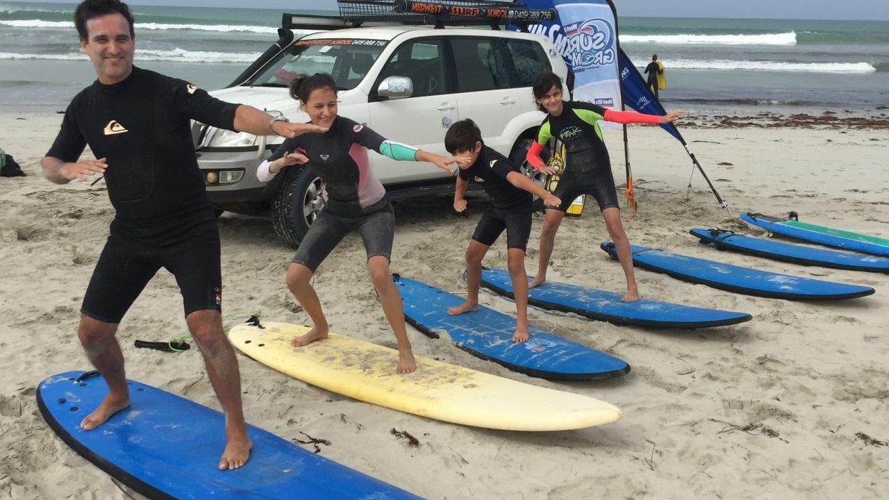 Surf lesson on beach with instructor and kids practicing on boards
