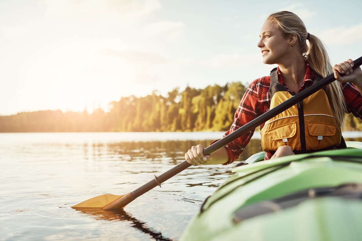 Woman paddling a kayak at golden sunrise on tranquil lake