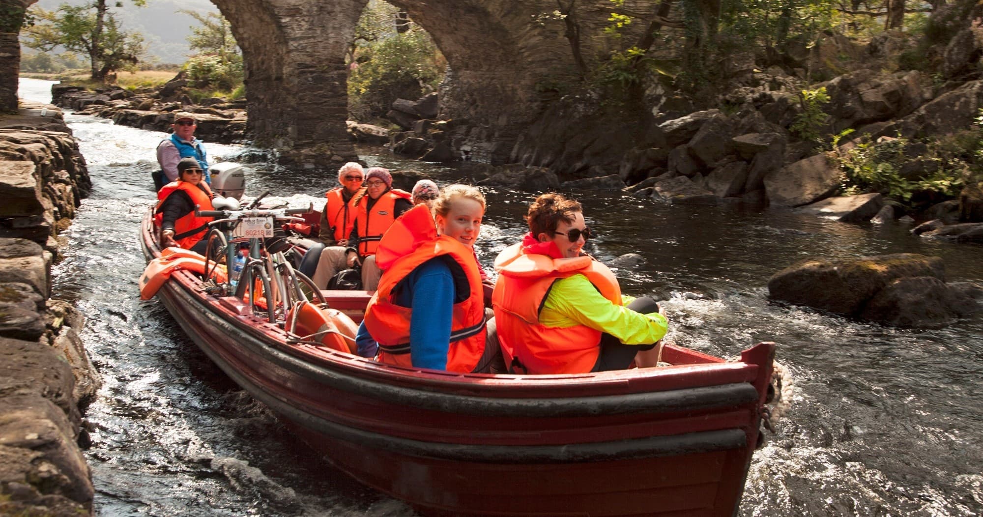 Group boat tour passing beneath a stone bridge on a river
