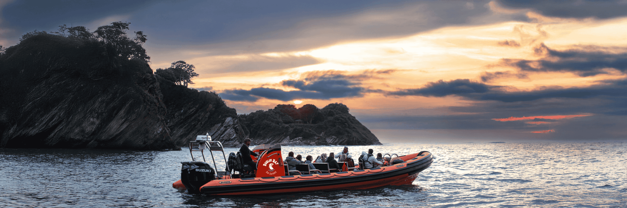 Rib boat tour at sea near rocky coastline at sunset