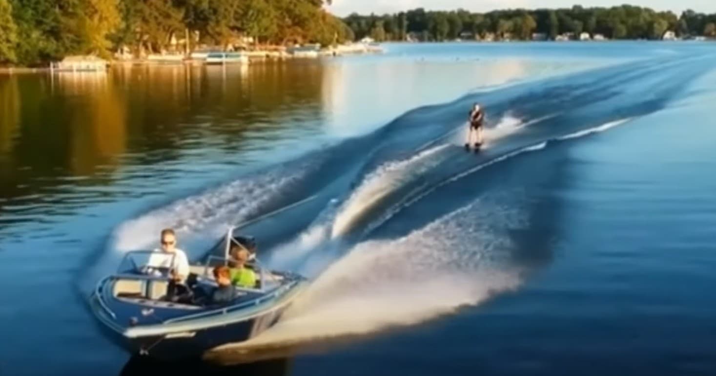 Speedboat carving wake across reflective forested lake at sunset