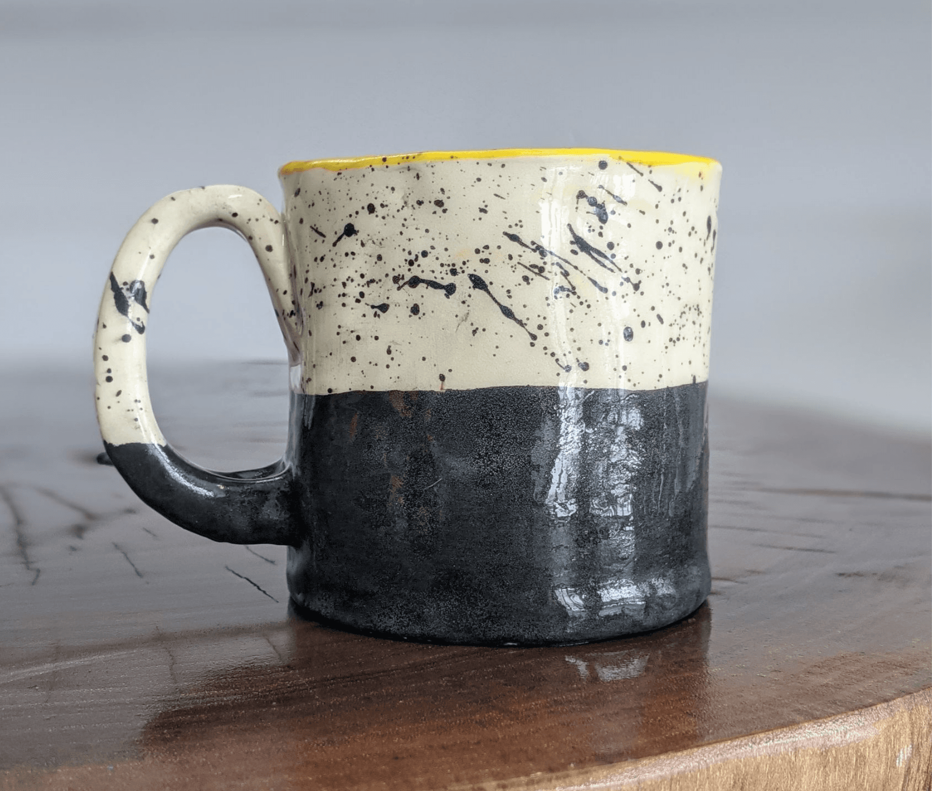 Handmade speckled ceramic mug on wooden table in studio setting