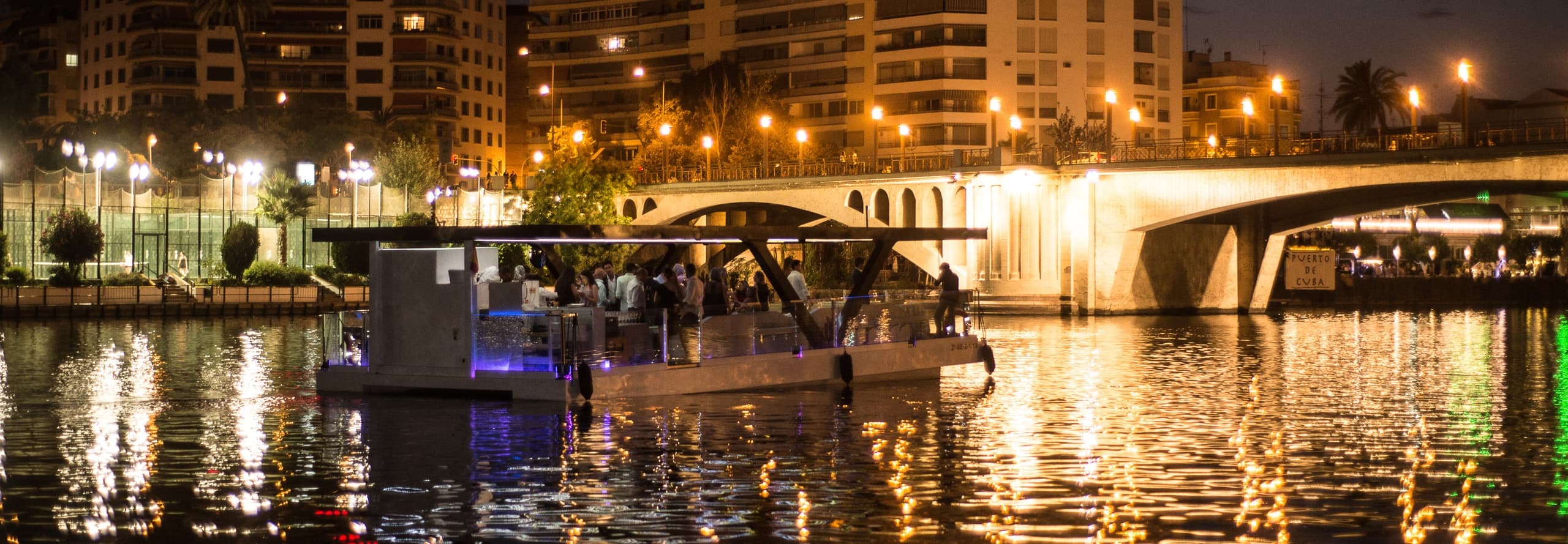 Evening river cruise passing illuminated city bridge at night
