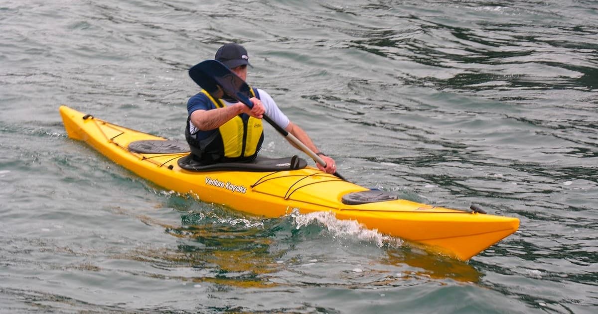 Solo kayaker paddling on choppy lake water, action shot