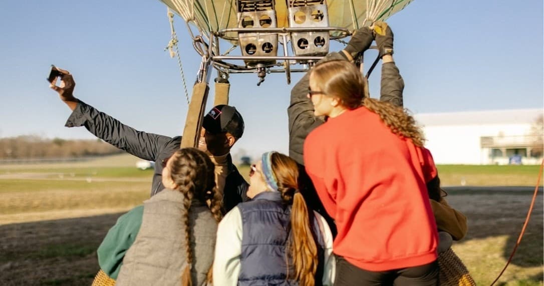 Passengers gathering at hot air balloon basket on grassy field