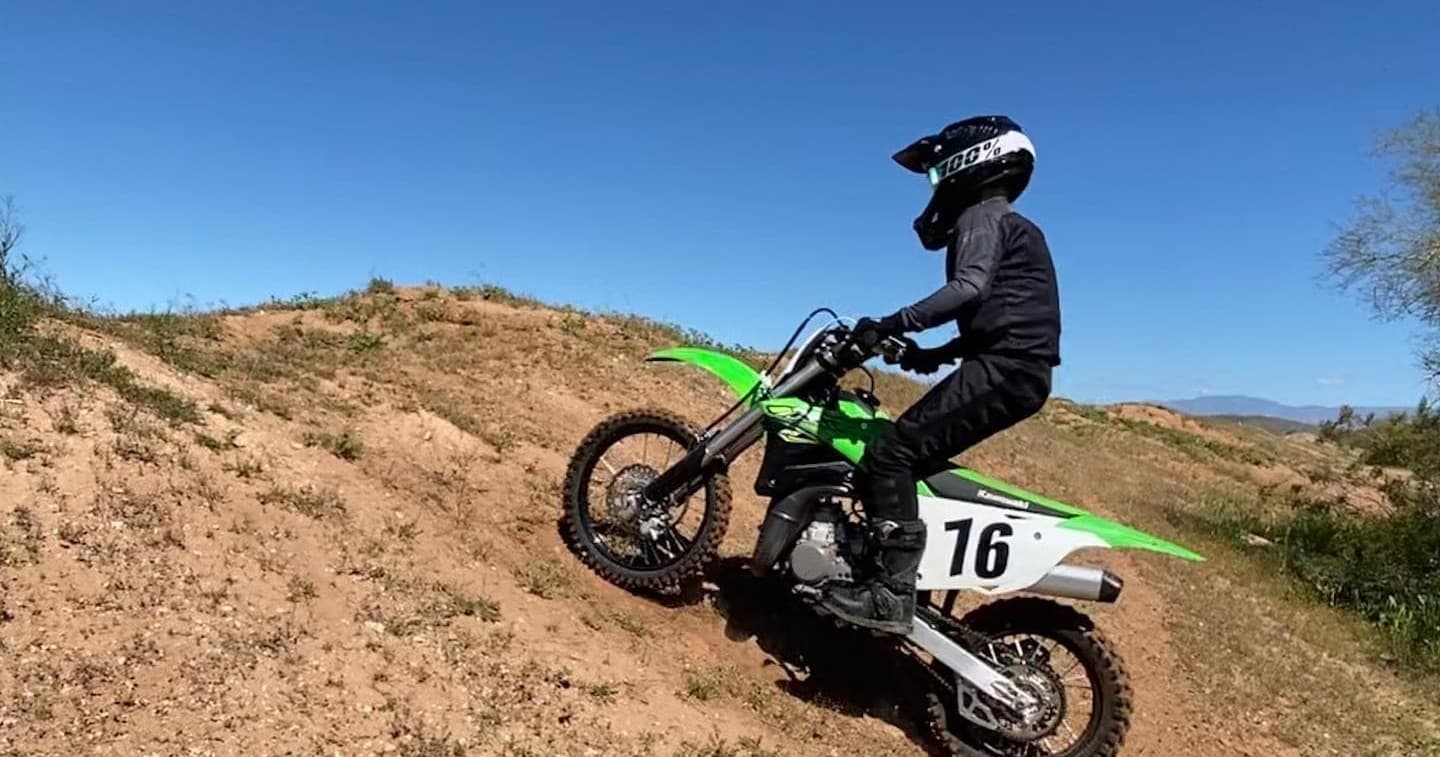 Rider on green dirt bike climbing sunlit desert hillside trail
