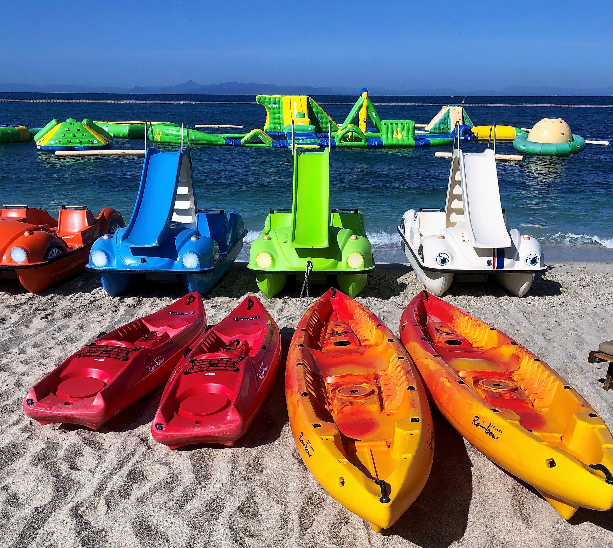 Colorful kayaks and pedal boats lined on sandy beach shore