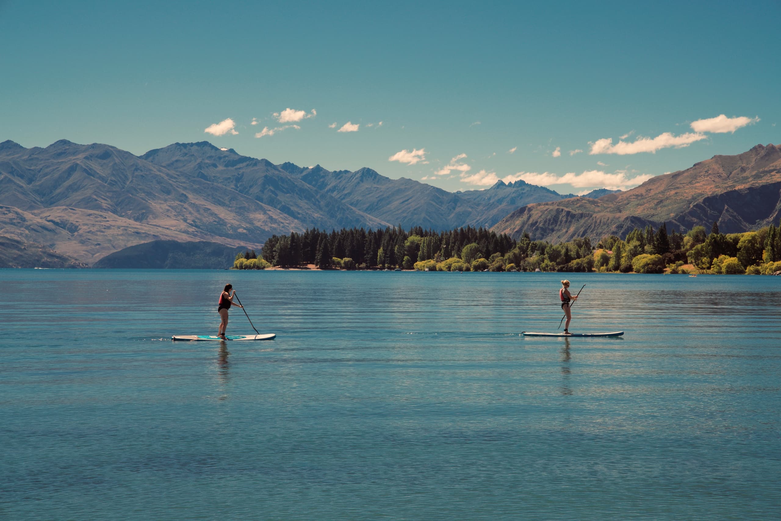 Two paddleboarders on alpine lake with mountain backdrop paddling