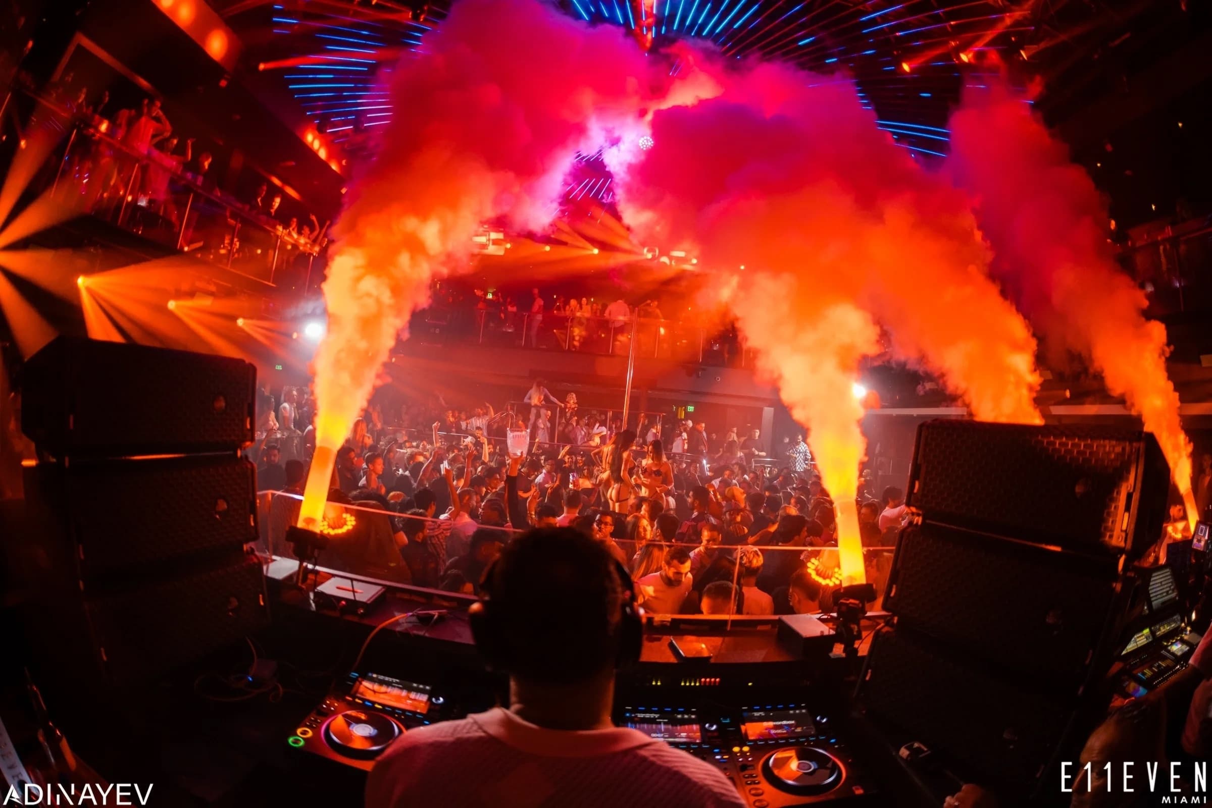 DJ performing in packed nightclub with pyrotechnic smoke show