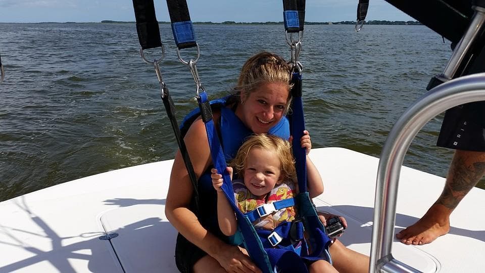 Parent and child seated in harness on boat deck during parasail prep