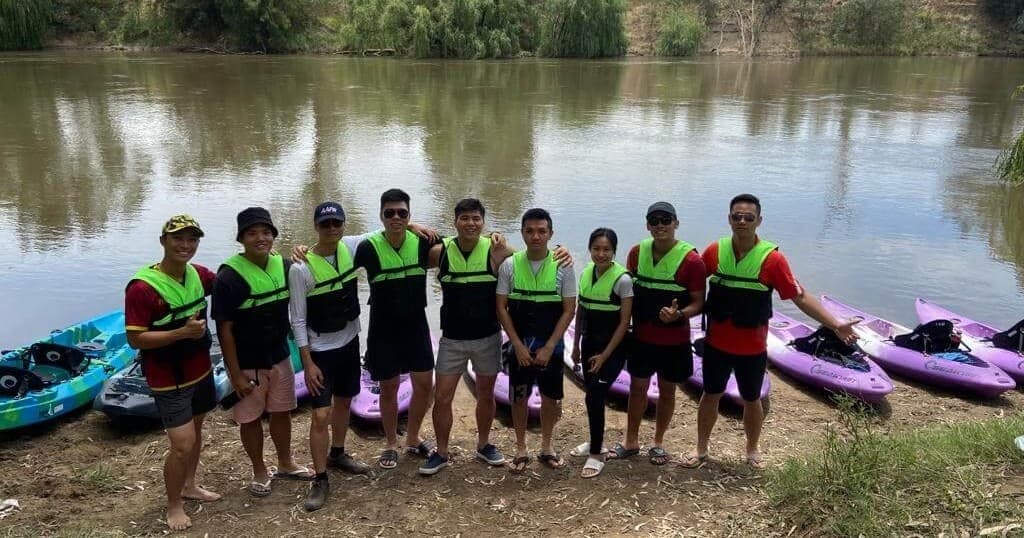 Group of paddlers in life vests standing by river with kayaks