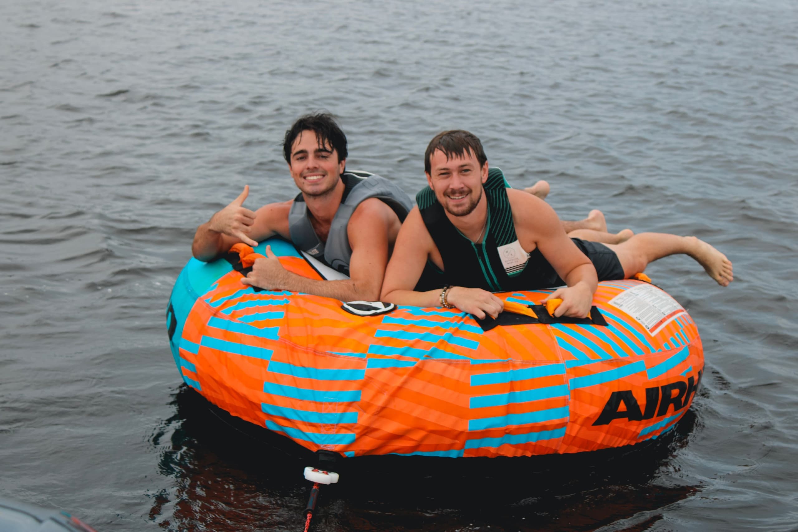 Two adults tubing on open water, holding onto inflatable tow tube