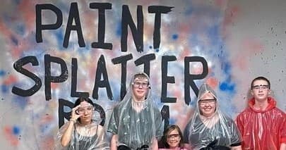 Group in paint splatter studio wearing ponchos for messy art fun
