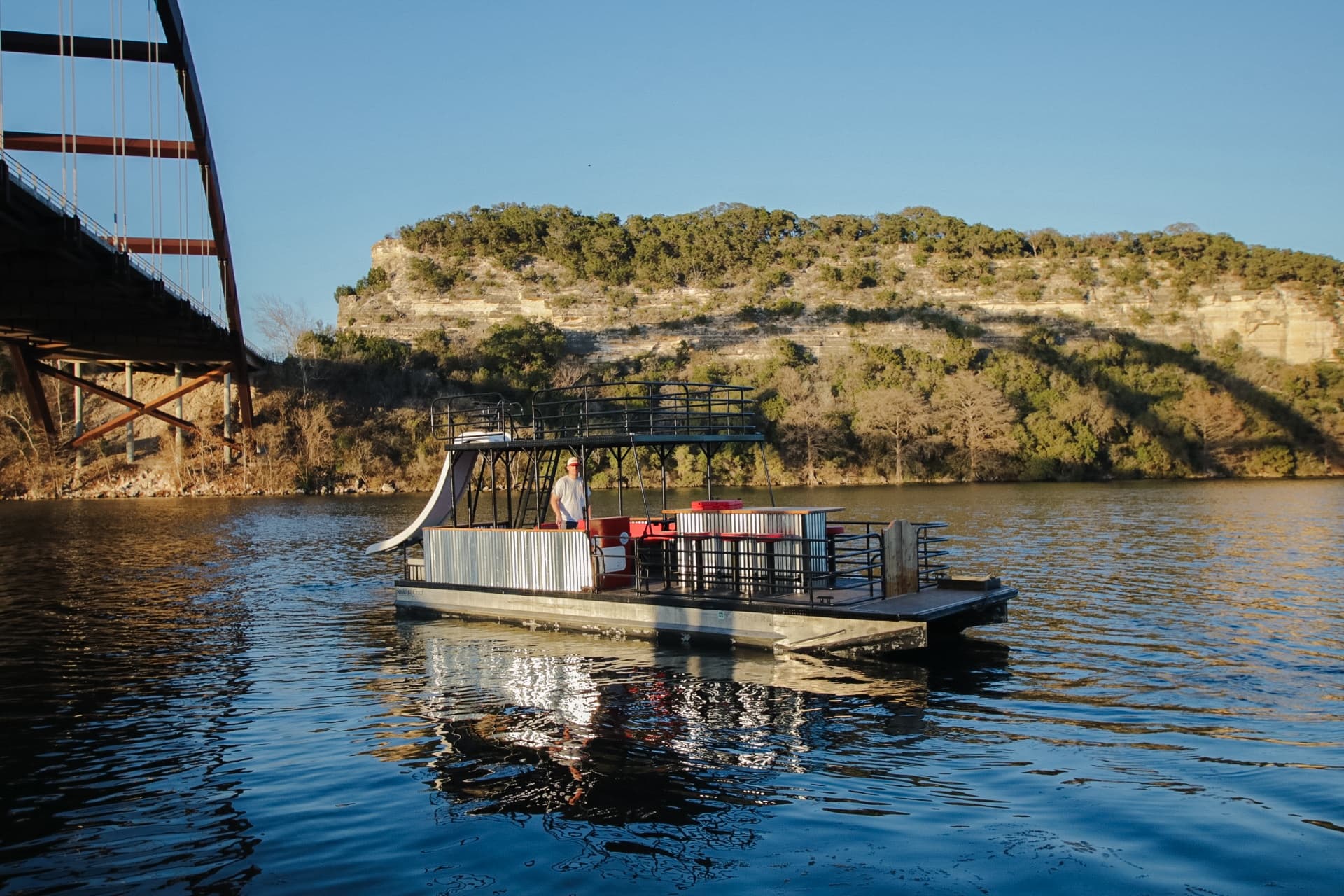 Pontoon boat cruising Lady Bird Lake in Austin with cliff and bridge