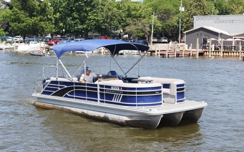 Blue pontoon boat gliding on waterfront with houses beyond