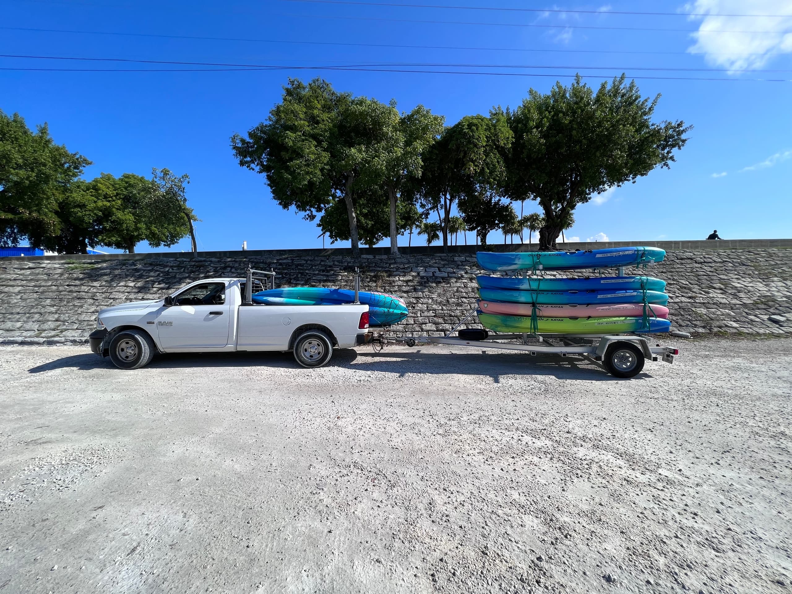 Pickup towing trailer stacked with colorful kayaks along Keys shoreline