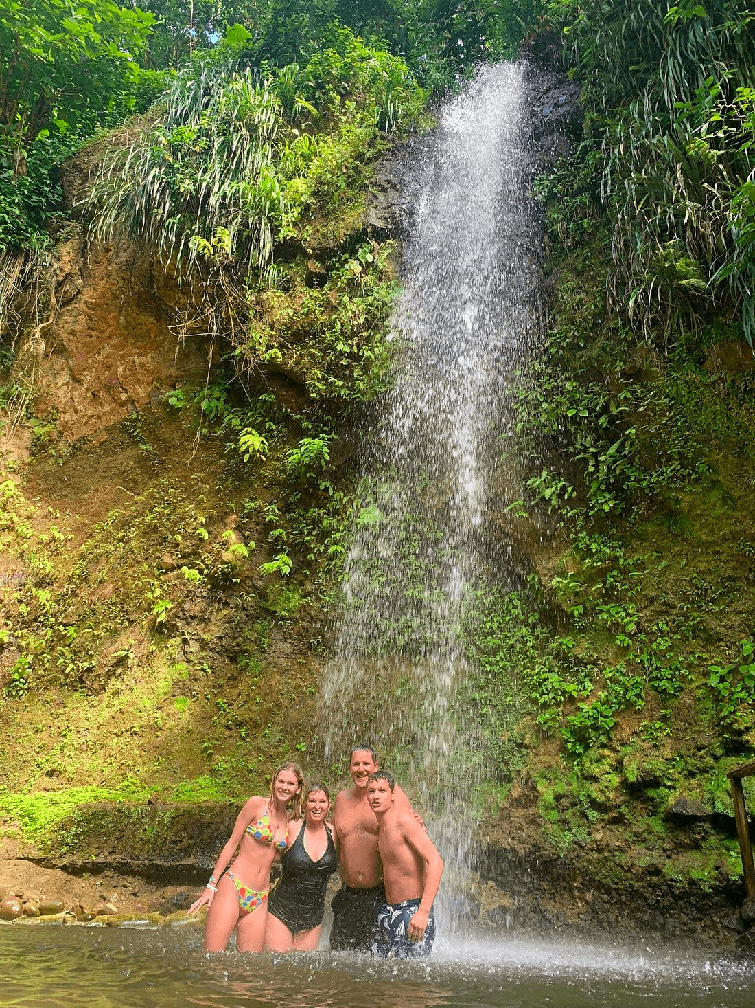 Couple posing under tropical waterfall in rainforest canyon