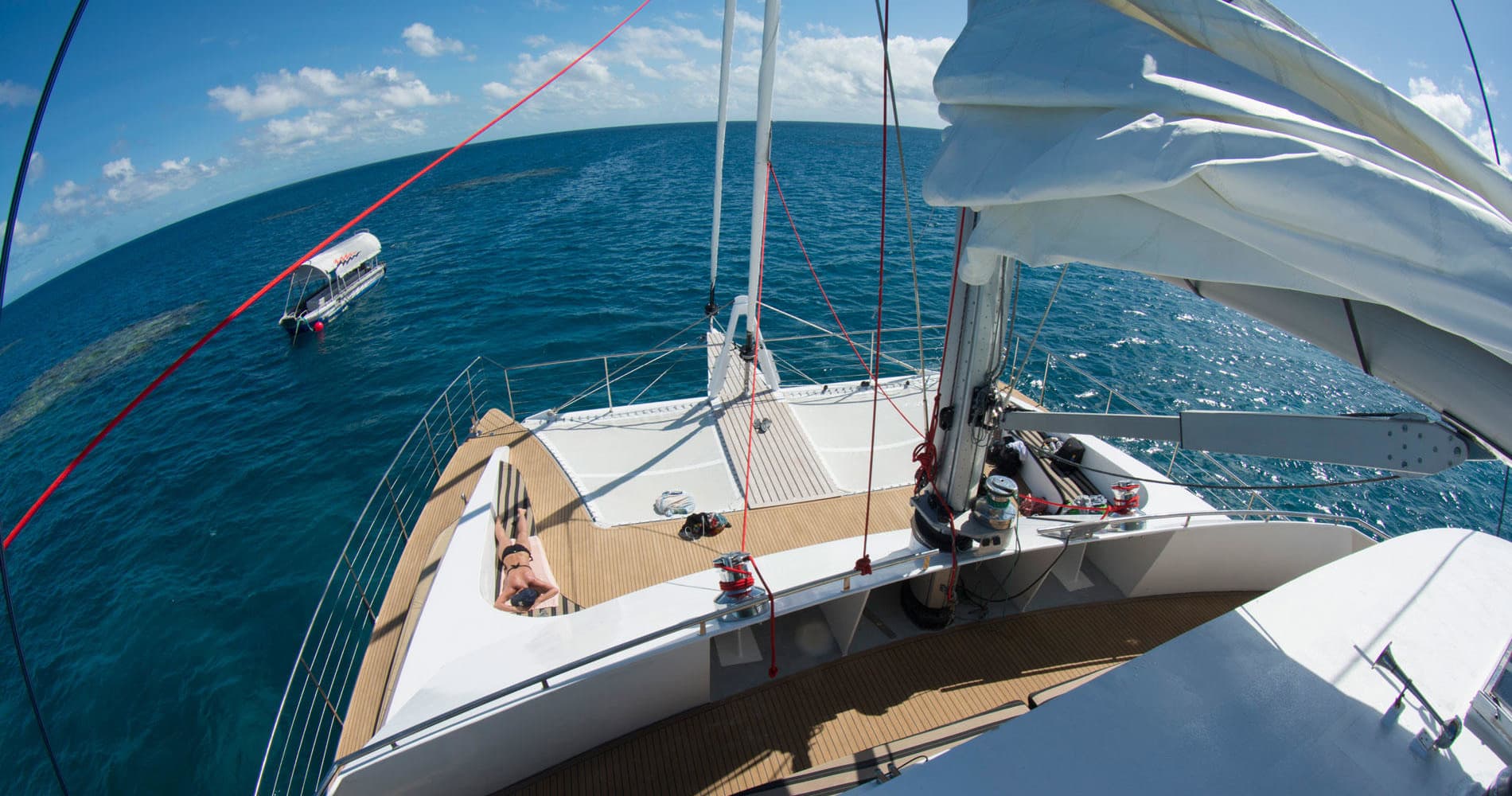 View from sailboat bow cruising on open ocean with sunbathers