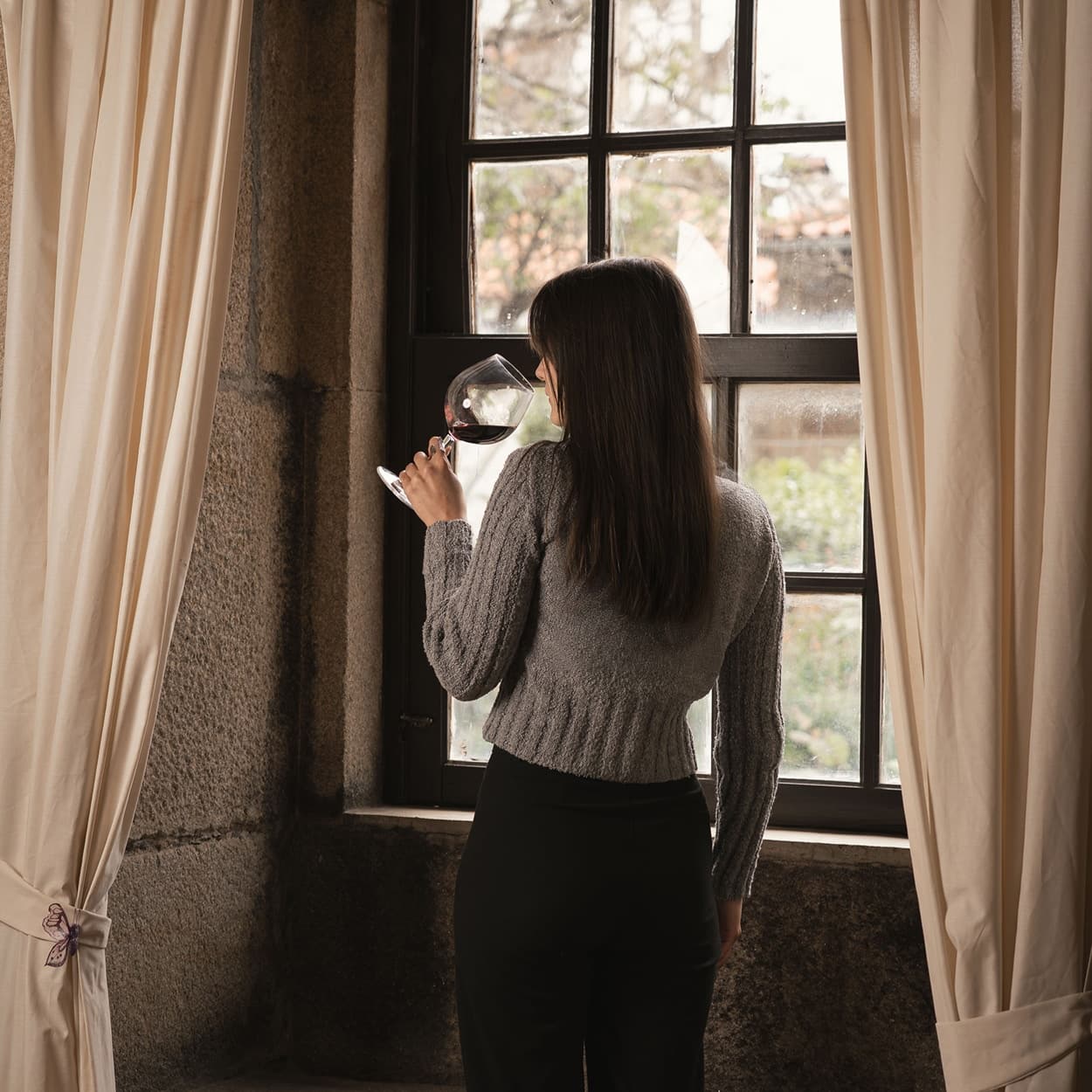 Woman tasting wine by rustic window in stone country guesthouse