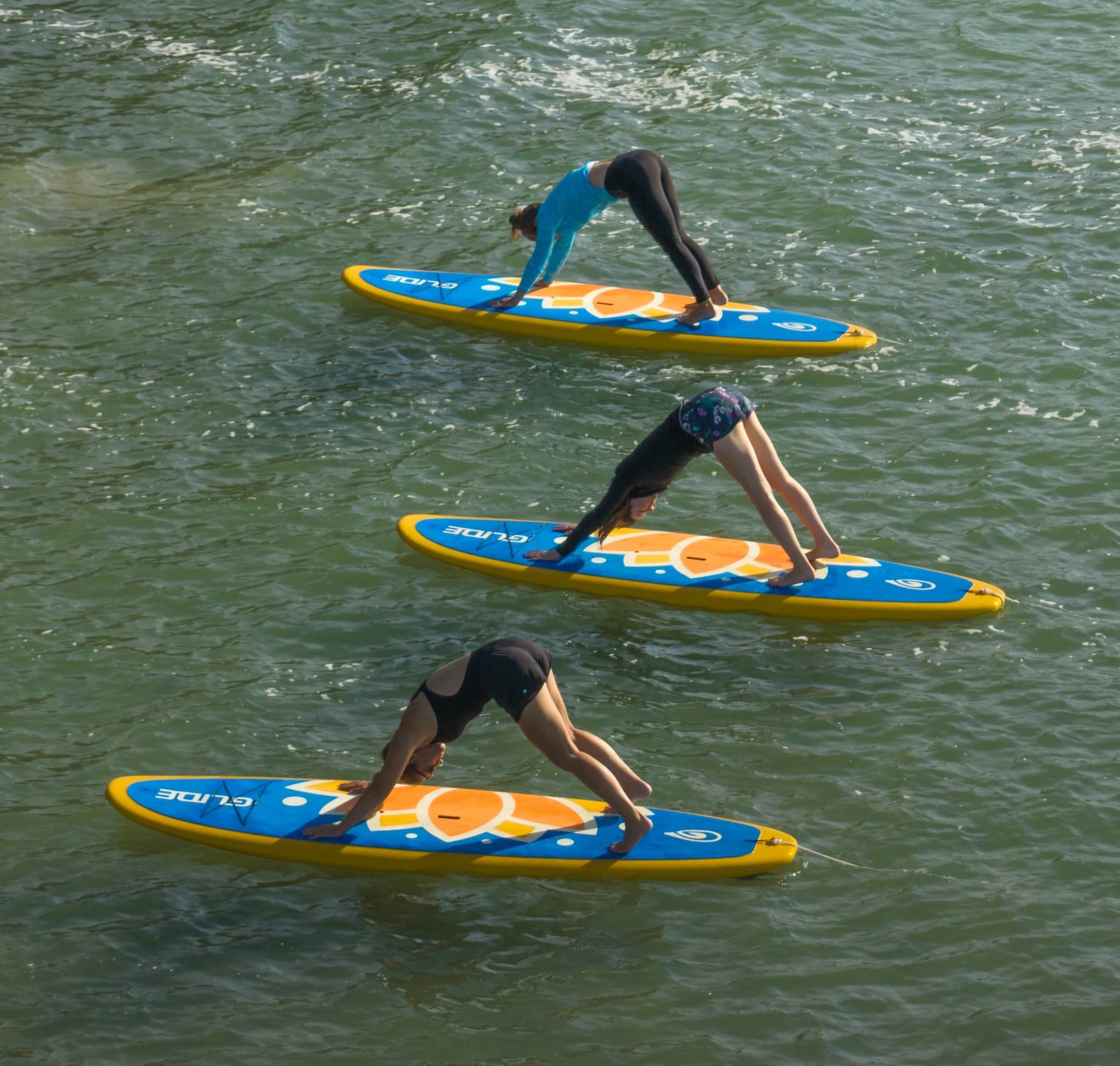 Three paddleboarders performing SUP yoga poses on river