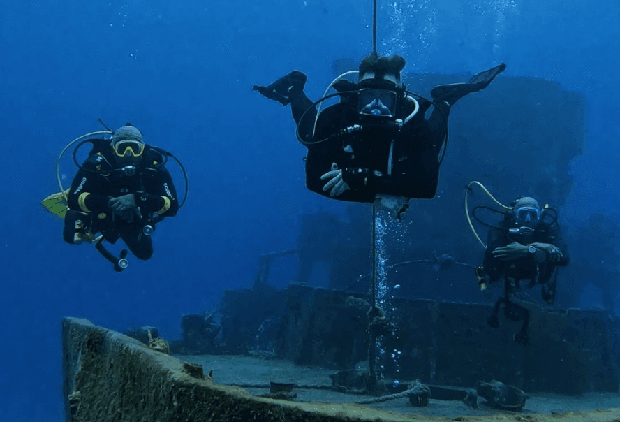 Group of scuba divers exploring submerged wreck site in ocean