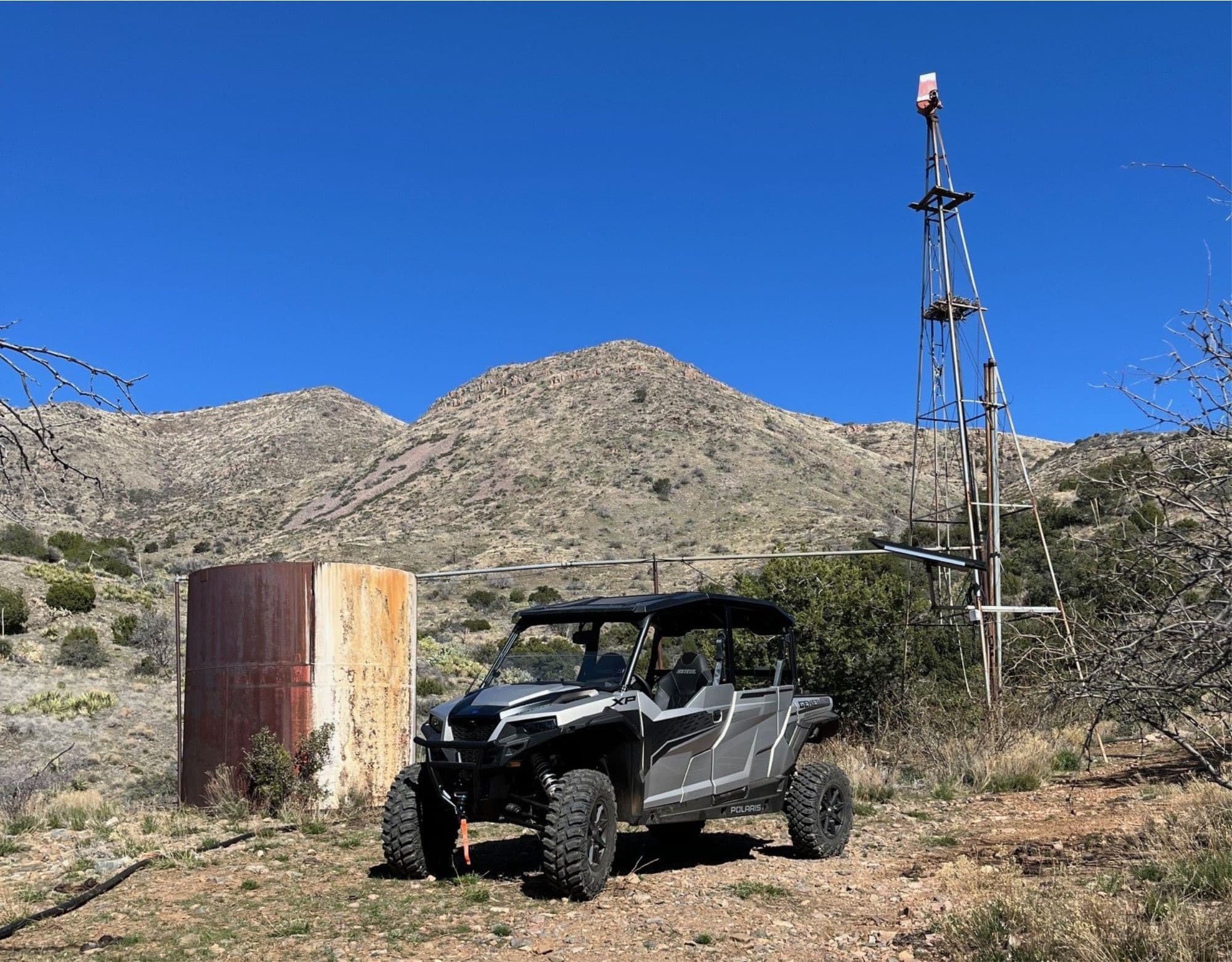 UTV parked by old windmill on desert hillside with mountains