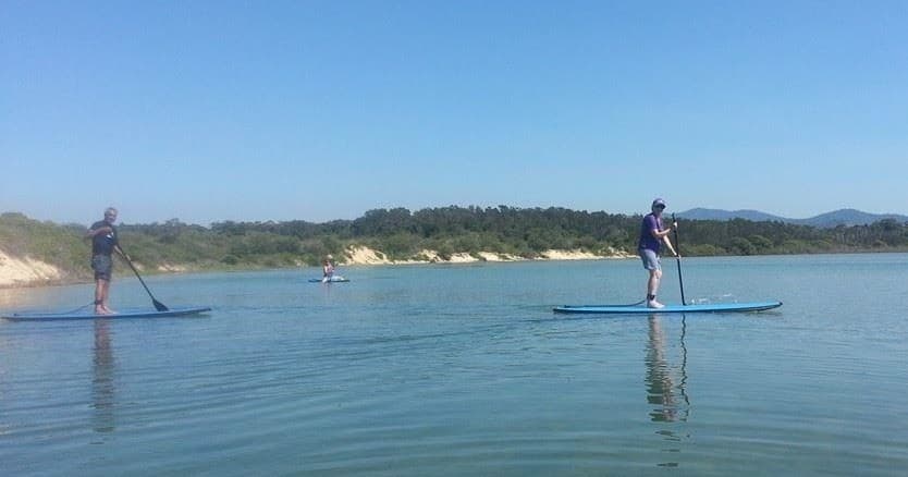 Stand-up paddleboarding on a calm coastal bay with distant hills