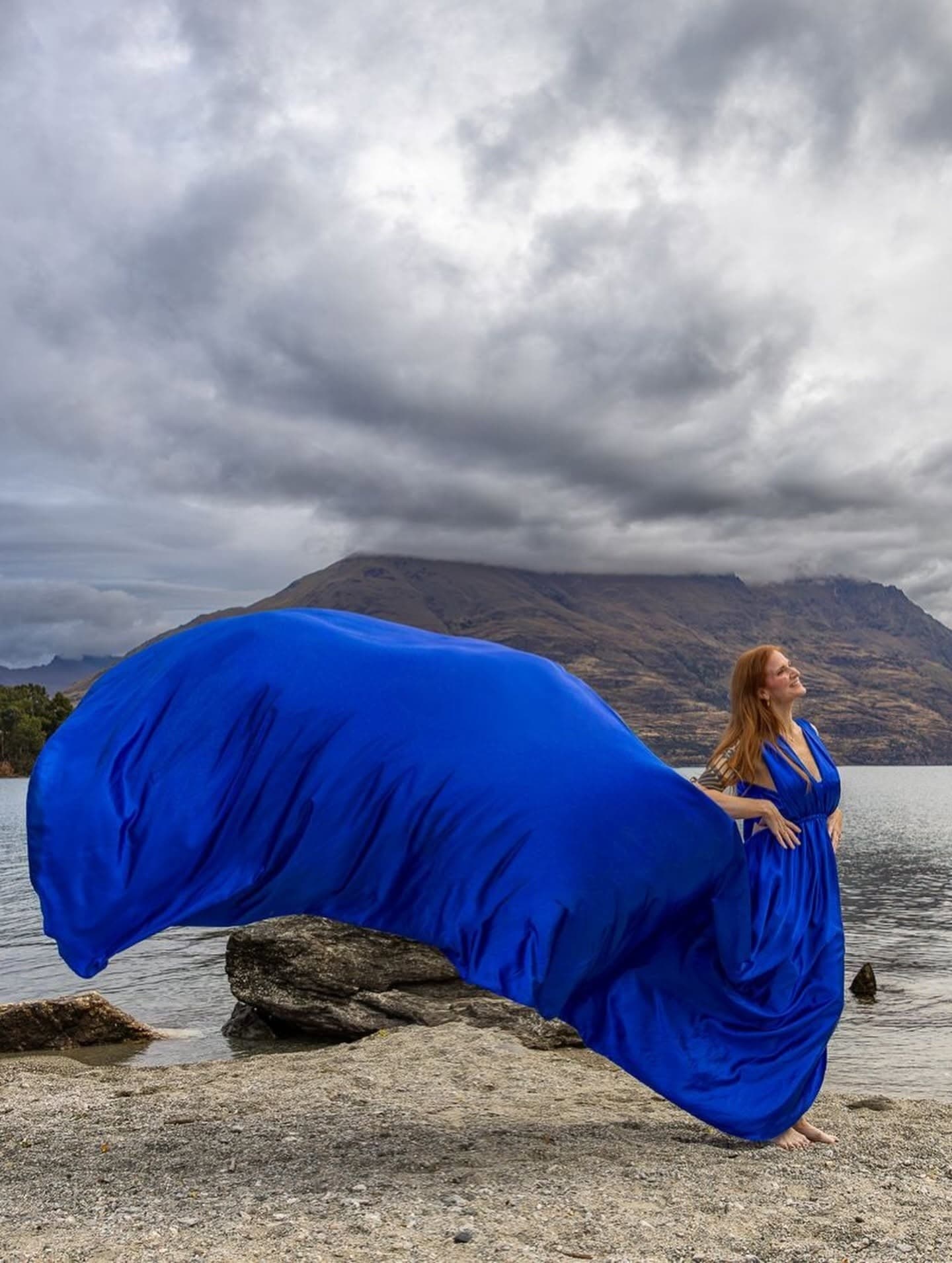 Blue dress swept by wind on coastal rock under dramatic sky