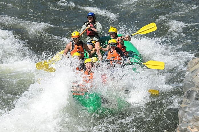 Raft plunging through heavy whitewater rapids on rocky river