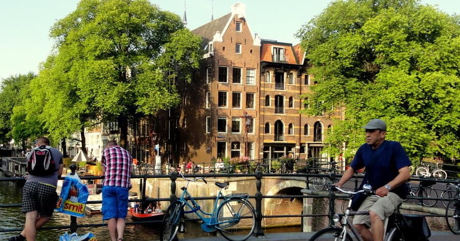 Cyclists and strollers on Amsterdam bridge over canal scene