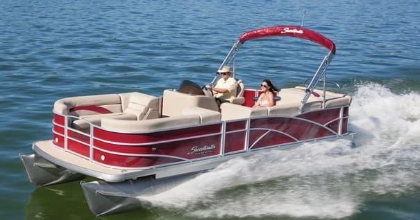 Red pontoon boat speeding over lake wake with passengers
