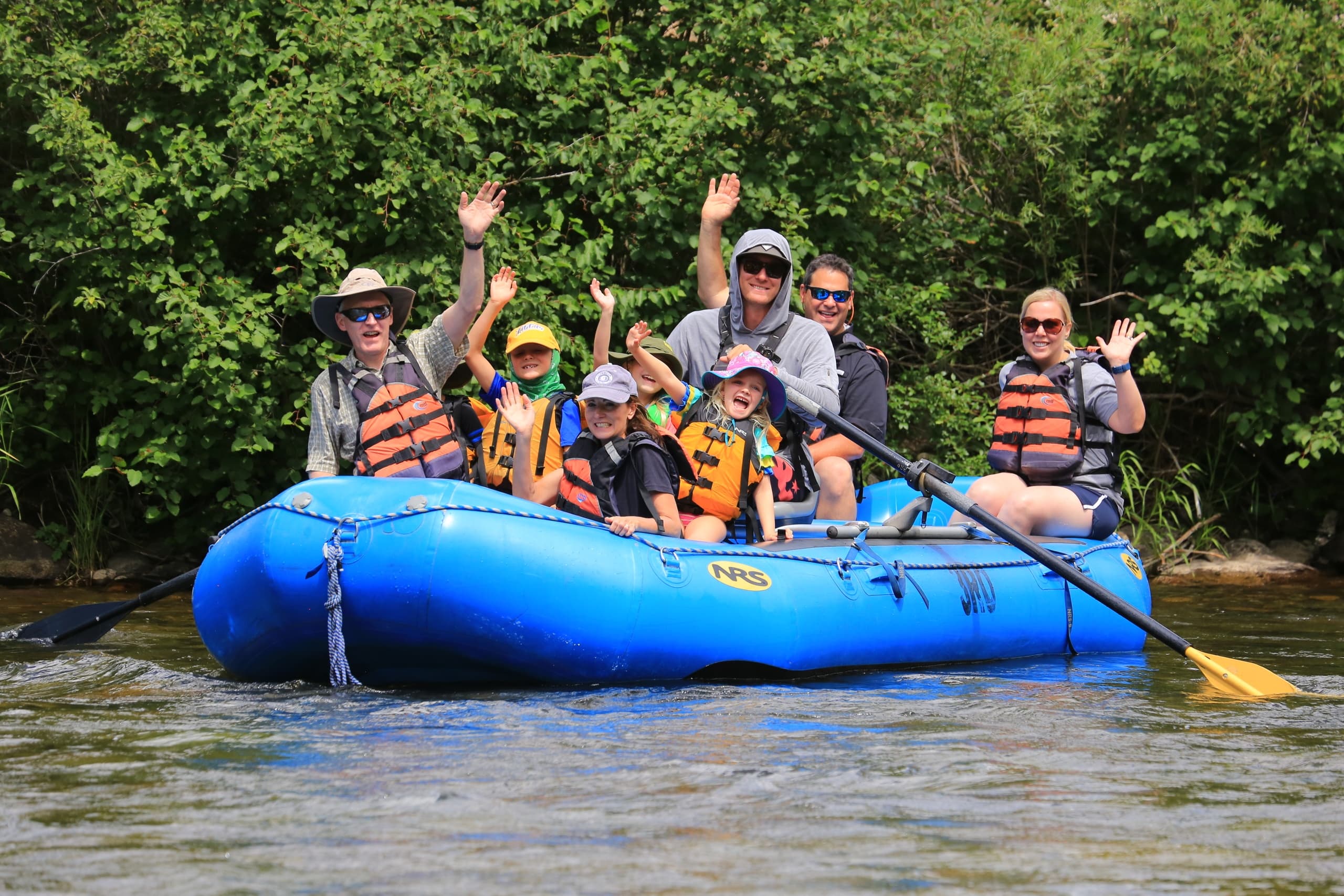 Group rafting on calm river with green canyon scenery waving