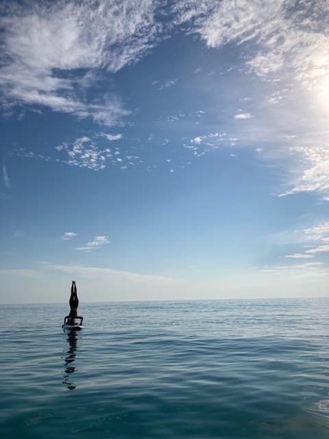 Stand-up paddleboarder balancing on calm open ocean at horizon