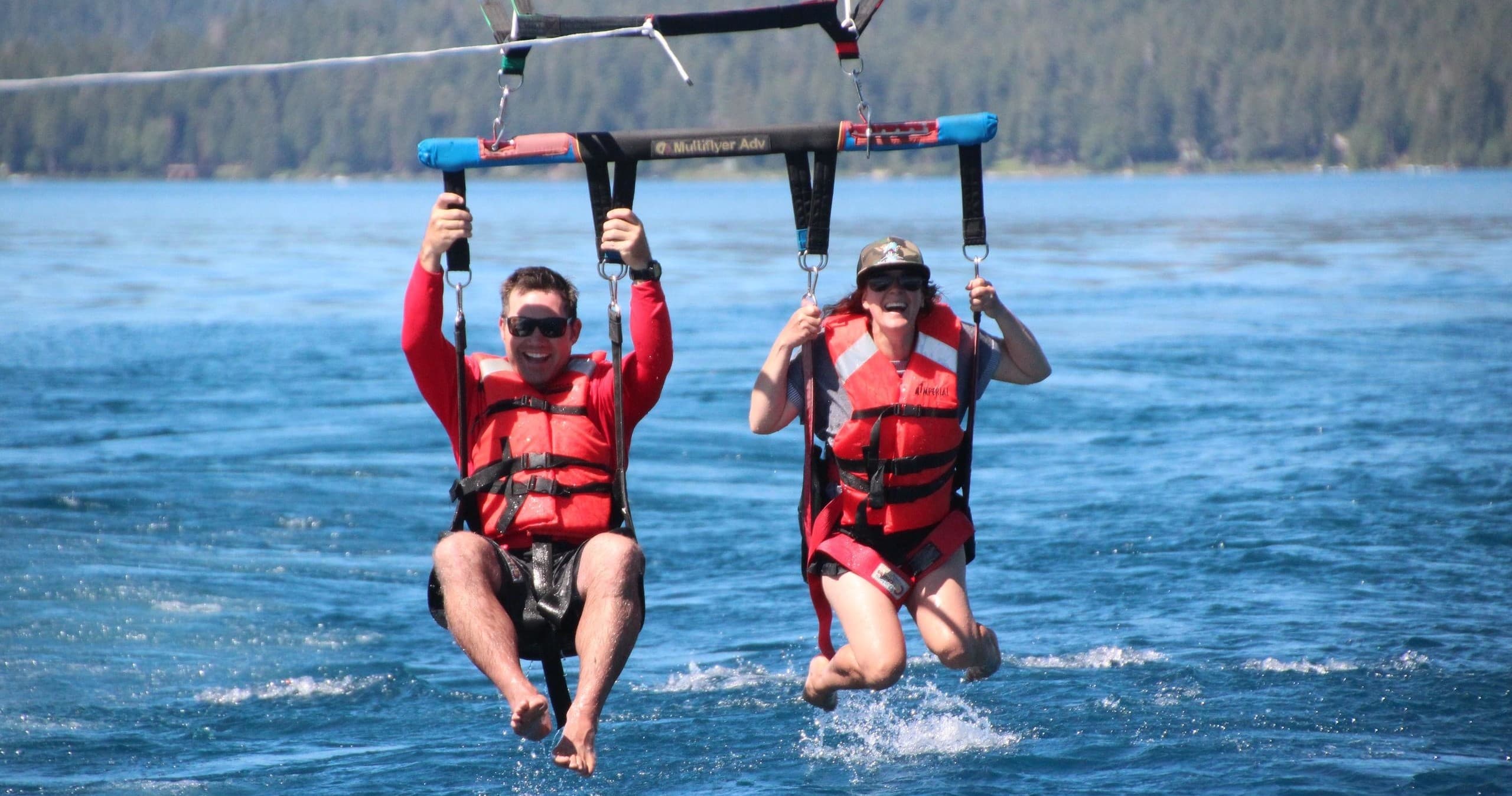 Two parasailers over blue lake waters near forested shoreline