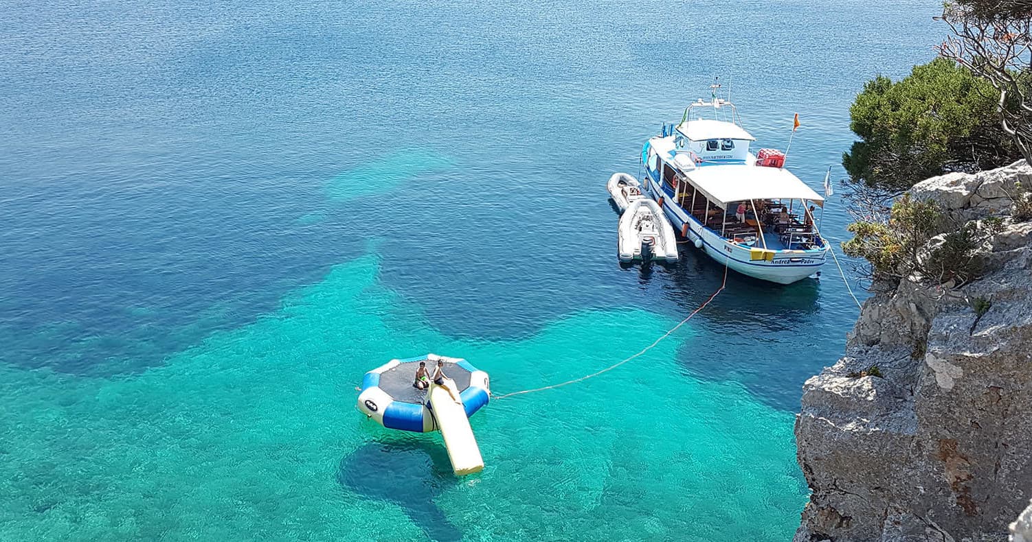 Small tour boat and dinghy in clear turquoise sea near cliffs
