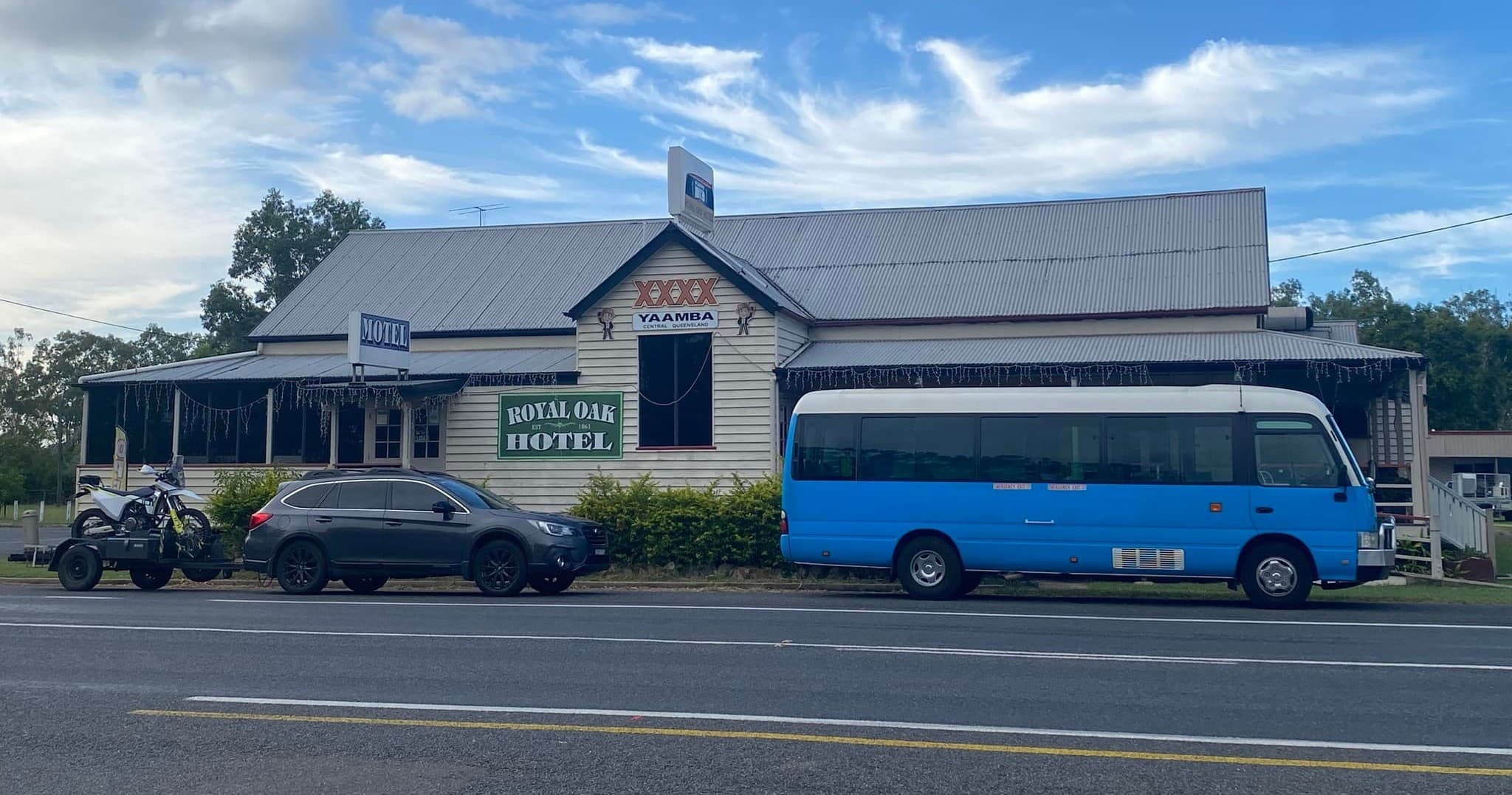 Blue tour minibus parked beside a riverside hotel, sunny sky