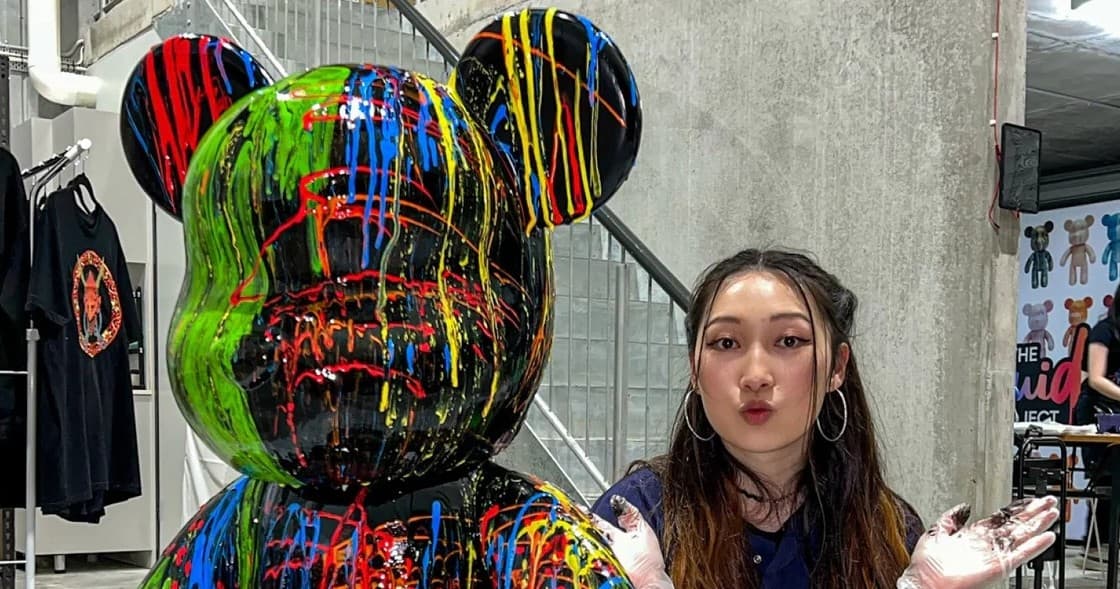 Artist beside large drip-painted bear sculpture in gallery