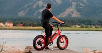 Rider on red electric fat-bike overlooking mountain lake