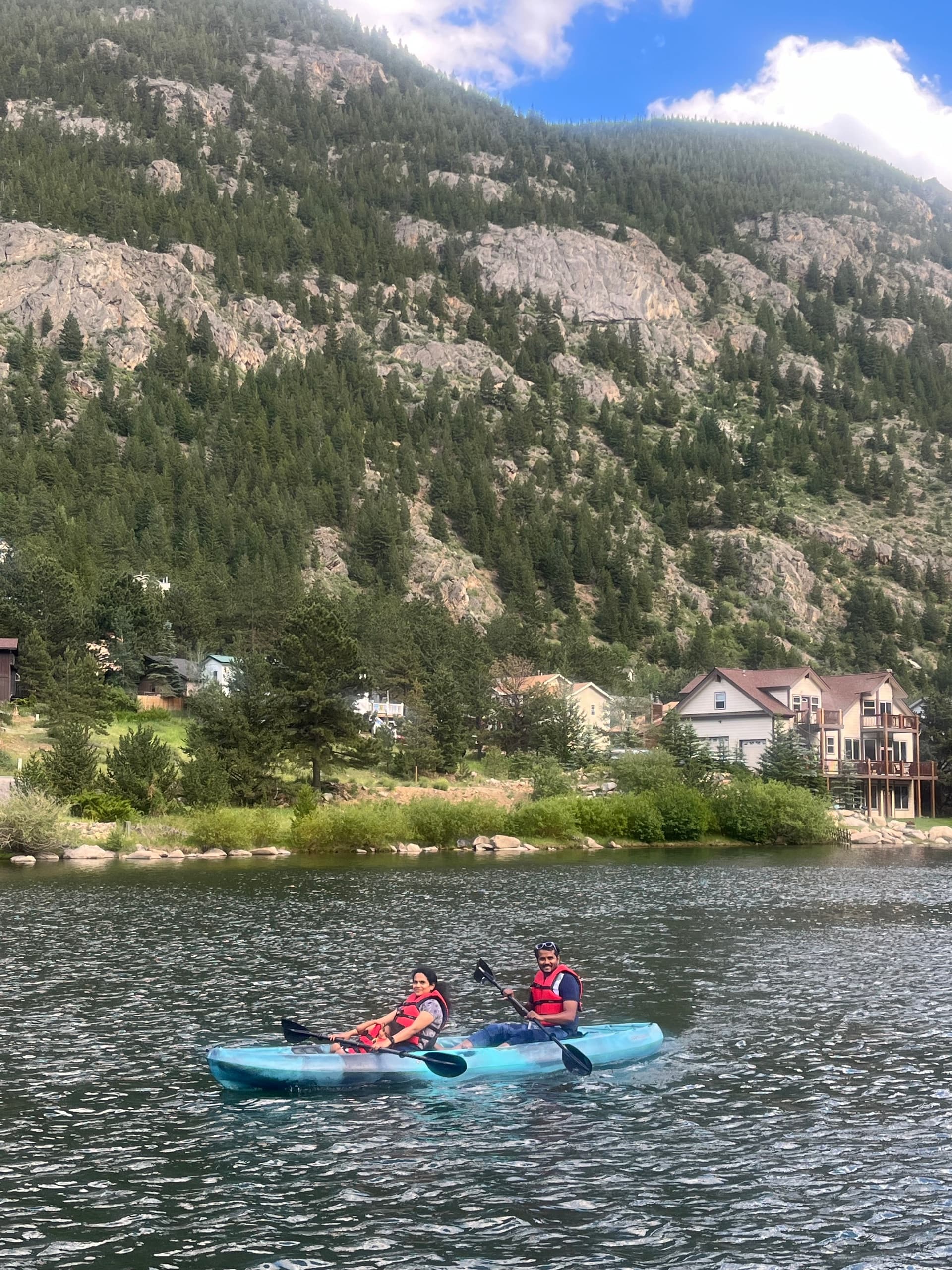 Two people kayaking on mountain lake near rocky shoreline