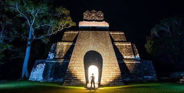 Silhouetted visitors at illuminated pyramid entrance at night