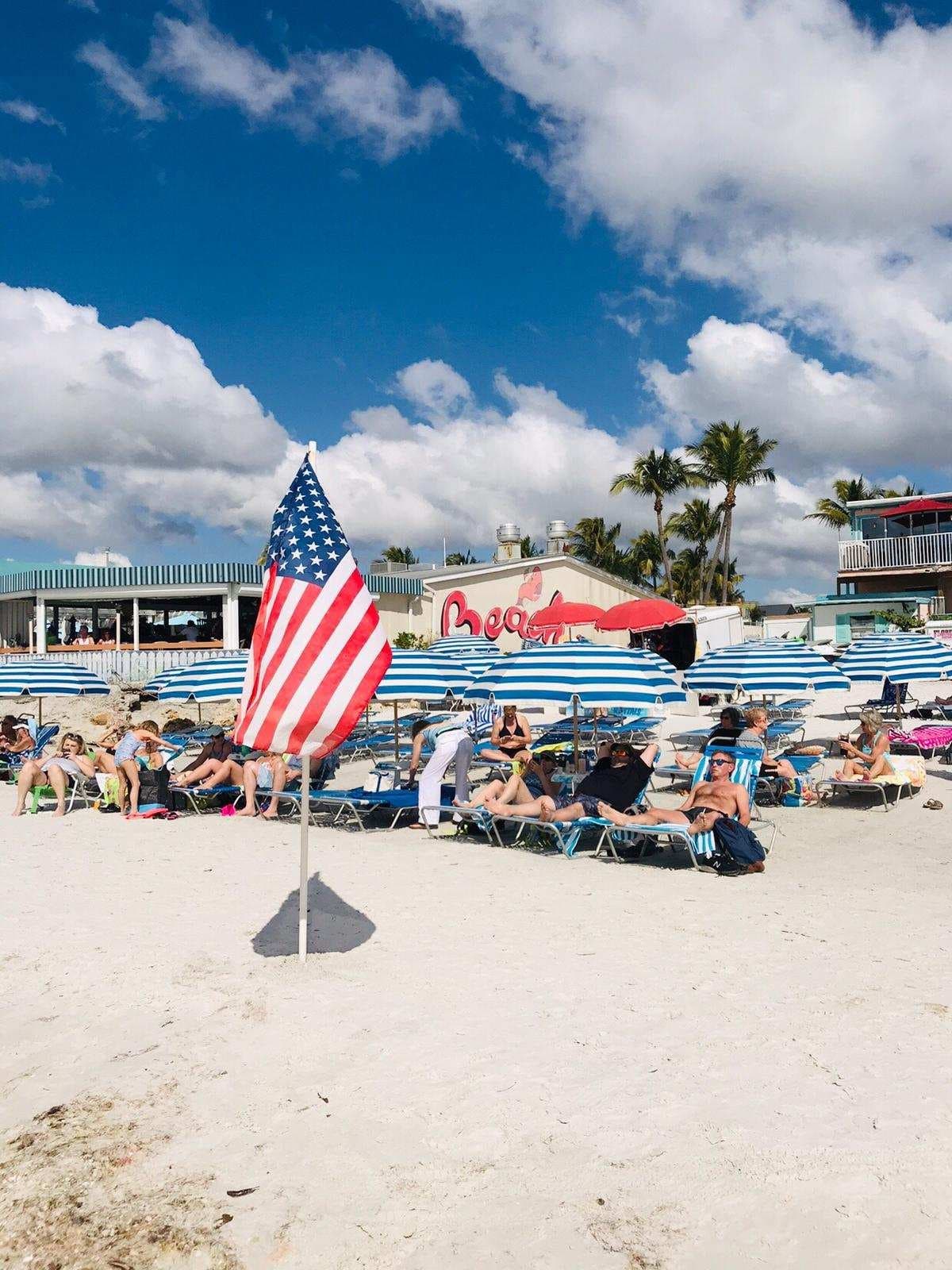 Beachgoers under American flag on sunny coastal beach, beachfront scene