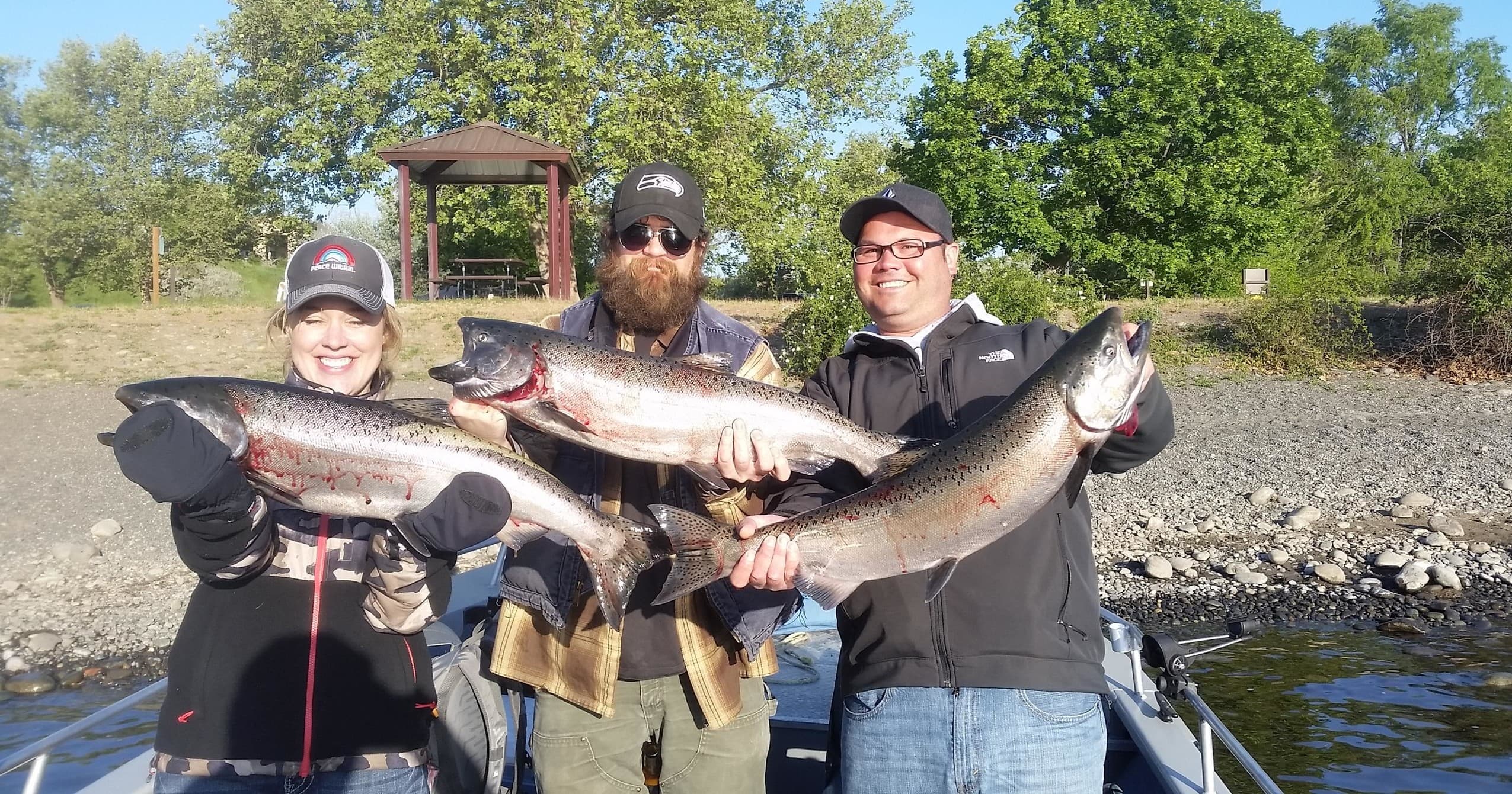 Three anglers displaying trophy salmon on boat, riverbank