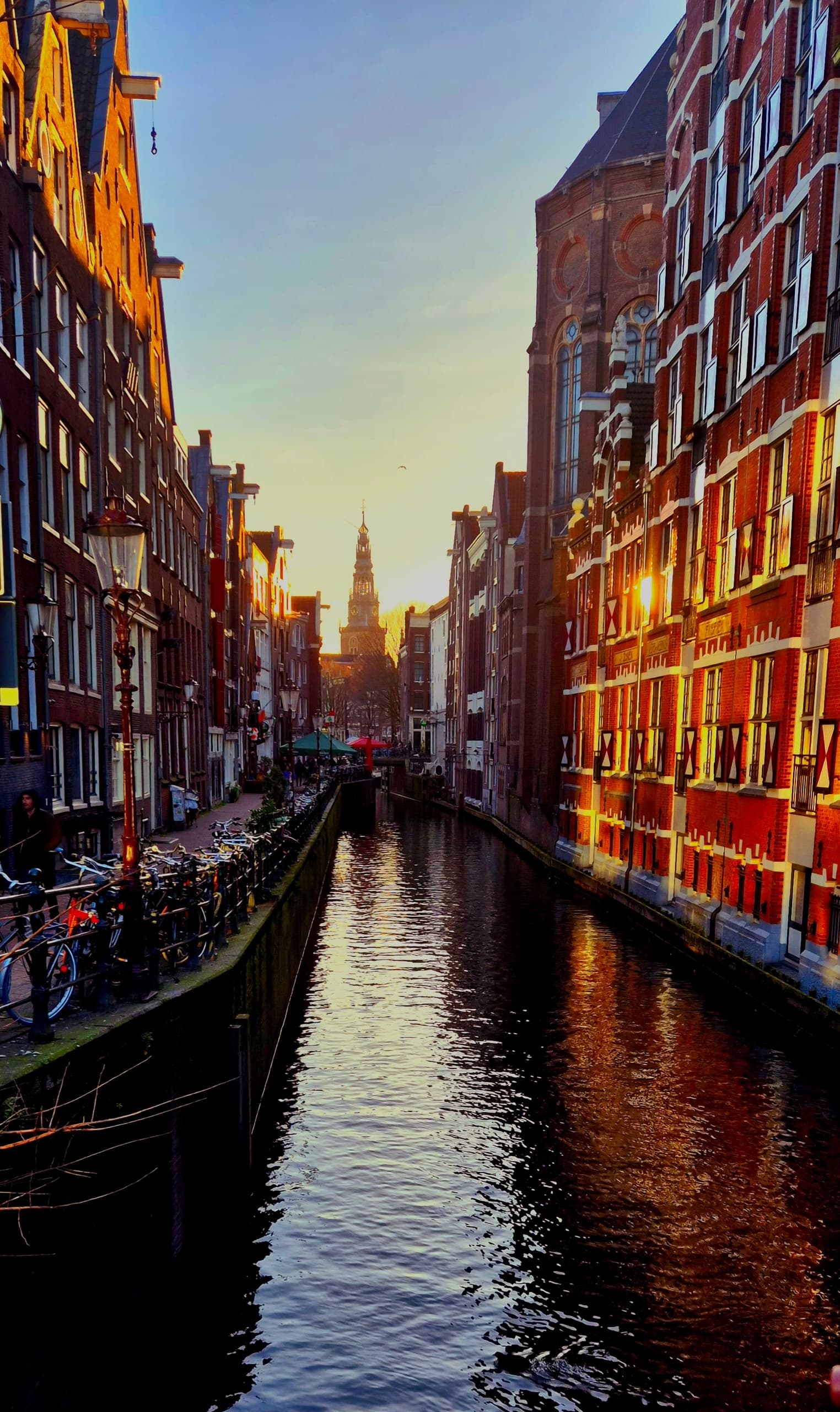 Sunlit Amsterdam canal lined with tall houses, scenic city boatway