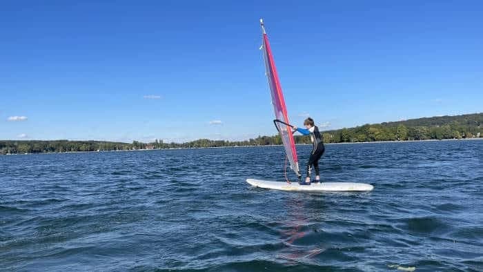 Single windsurfer on open lake under bright blue sky
